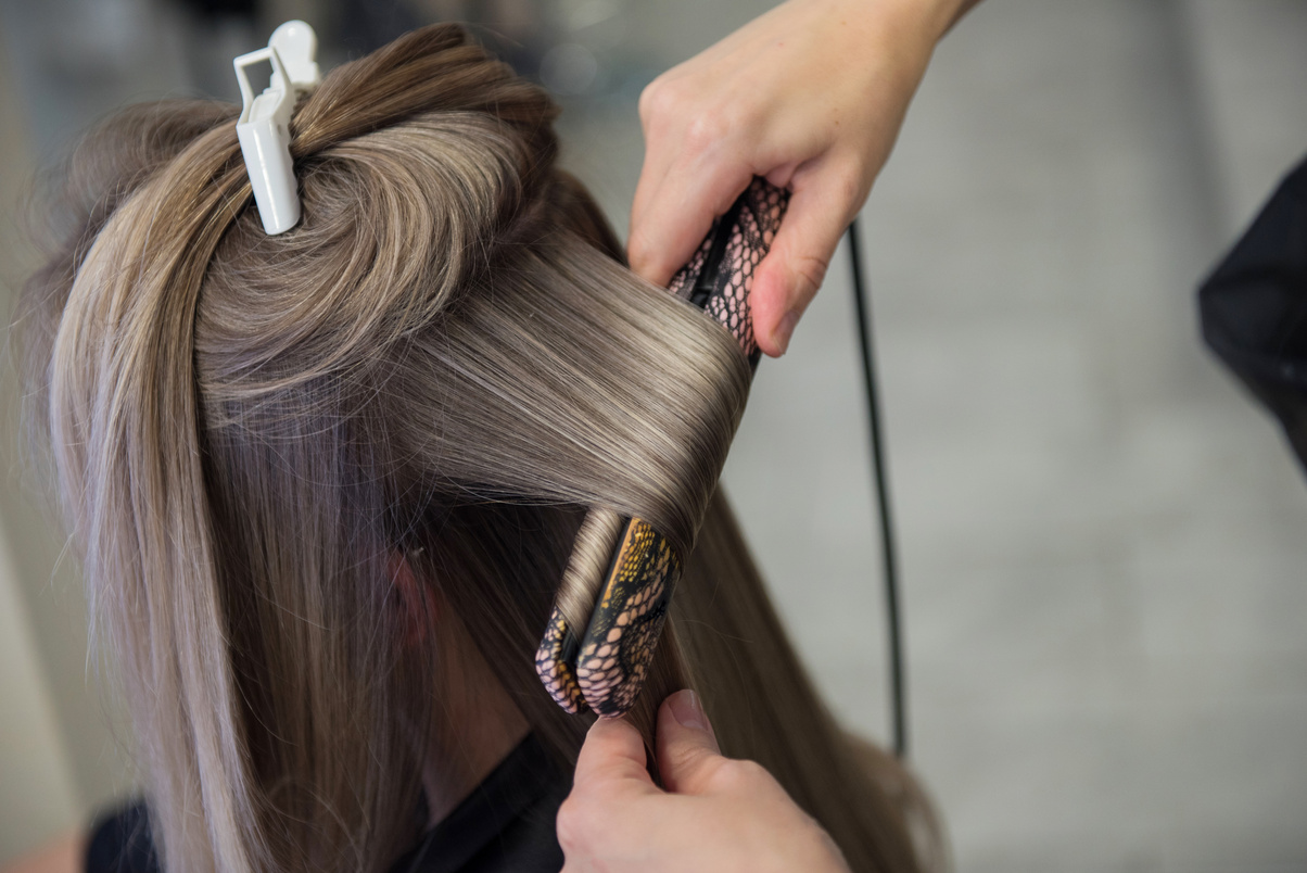 Young woman with beautiful highlights on her hair getting hair straighten in a hair salon